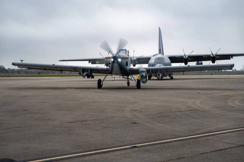 A Skyraider II is parked on an apron in front of a C-130