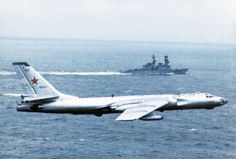 Soviet TU-16 flying over the water with a naval vessel in the background. 