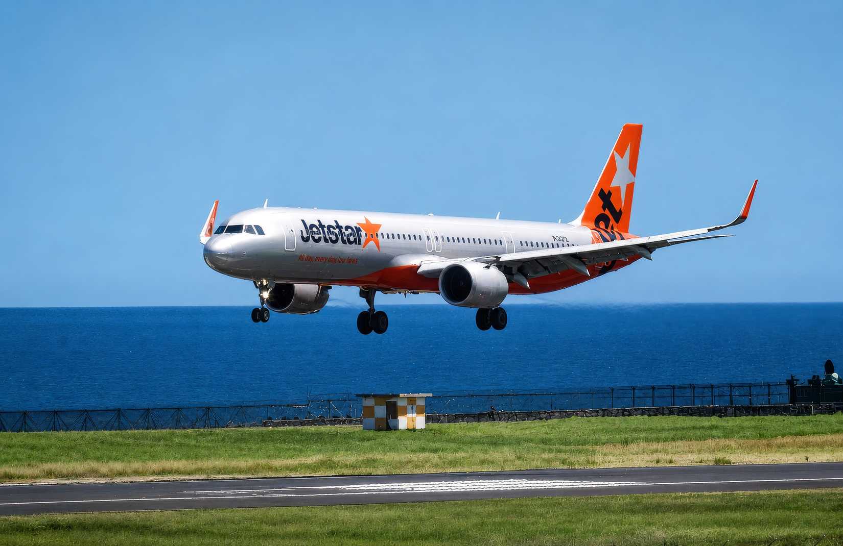 A Jetstar Airbus A321 commercial airplane preparing for landing on a runway near the coast.