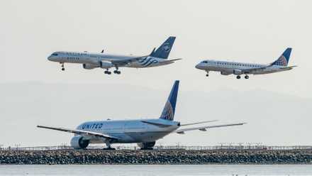 A United Airlines plane and Delta Airlines (with SkyTeam livery) plane come into land while a United Airlines plane waits at the end of the runway, 2018.