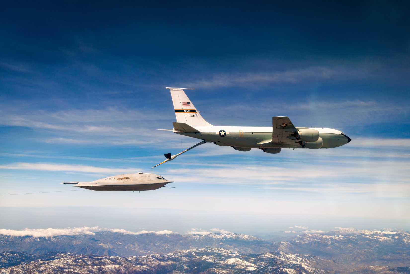 A photo of a B-21 engaging in aerial refueling with a mountain range in the background.
