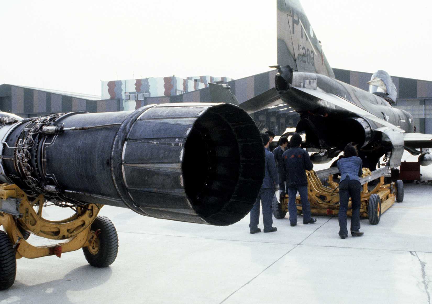 Korean specialists and Air Force maintenance technicians remove an engine from an F-4 Phantom II aircraft at the F-4 maintenance depot.