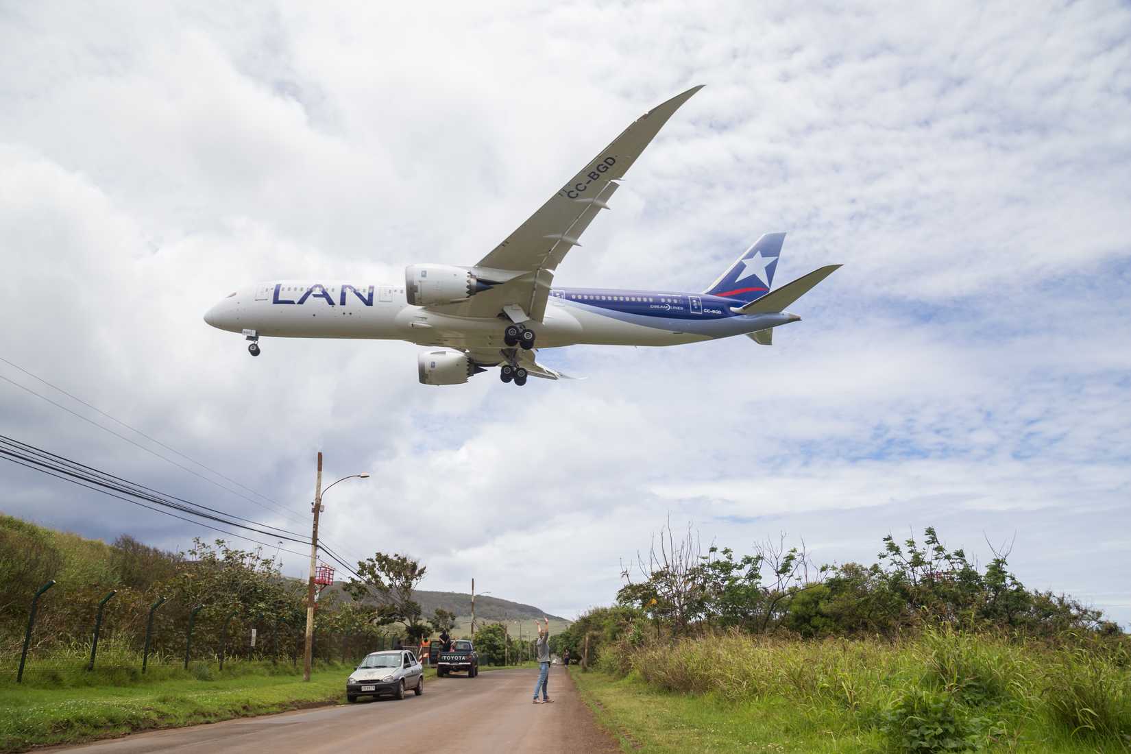 Photograph of a Boeing 787 Dreamliner landing on Easter Island while people are watching.