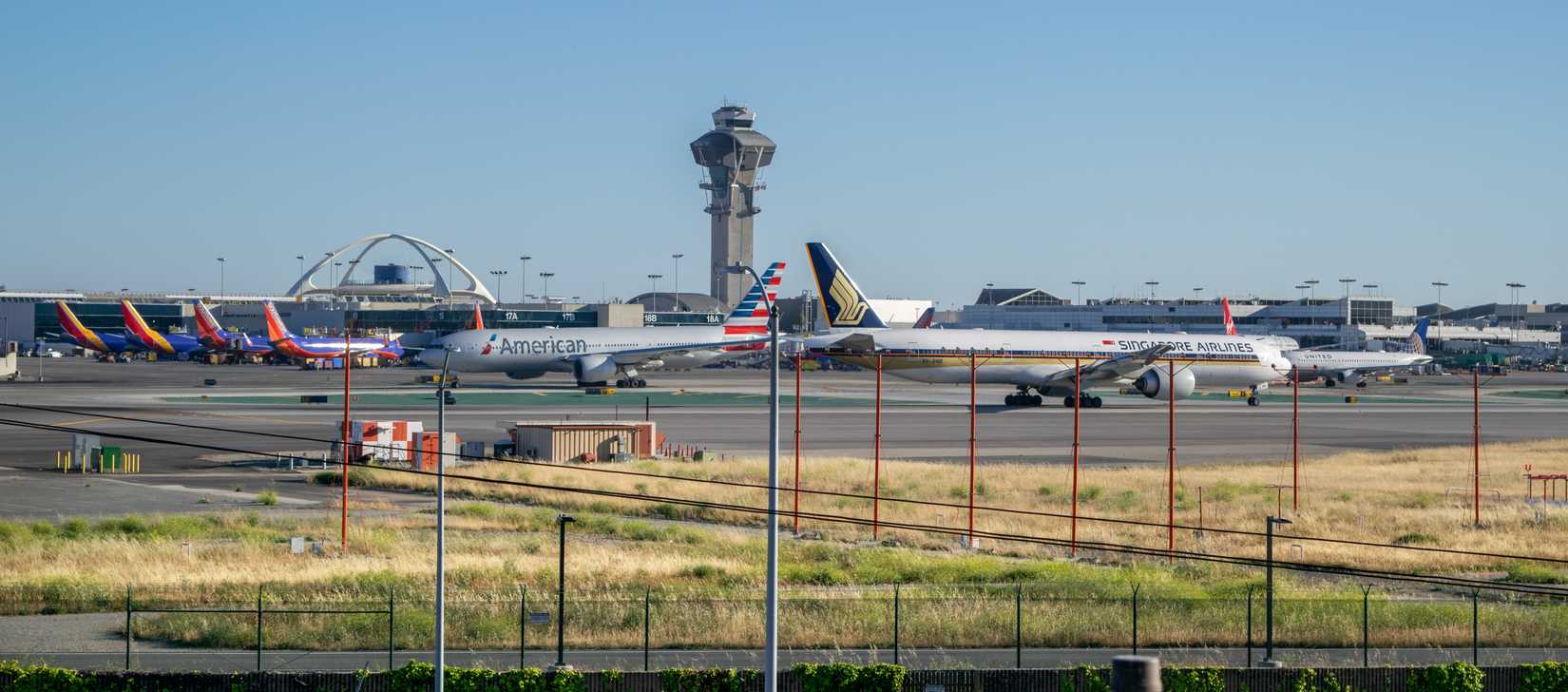 Los Angeles, California, USA - May 21, 2017: View of Singapore Airlines Boeing 777 stands ready for takeoff while an American Airlines Boeing 777 taxis to the runway, with iconic Theme Building behind