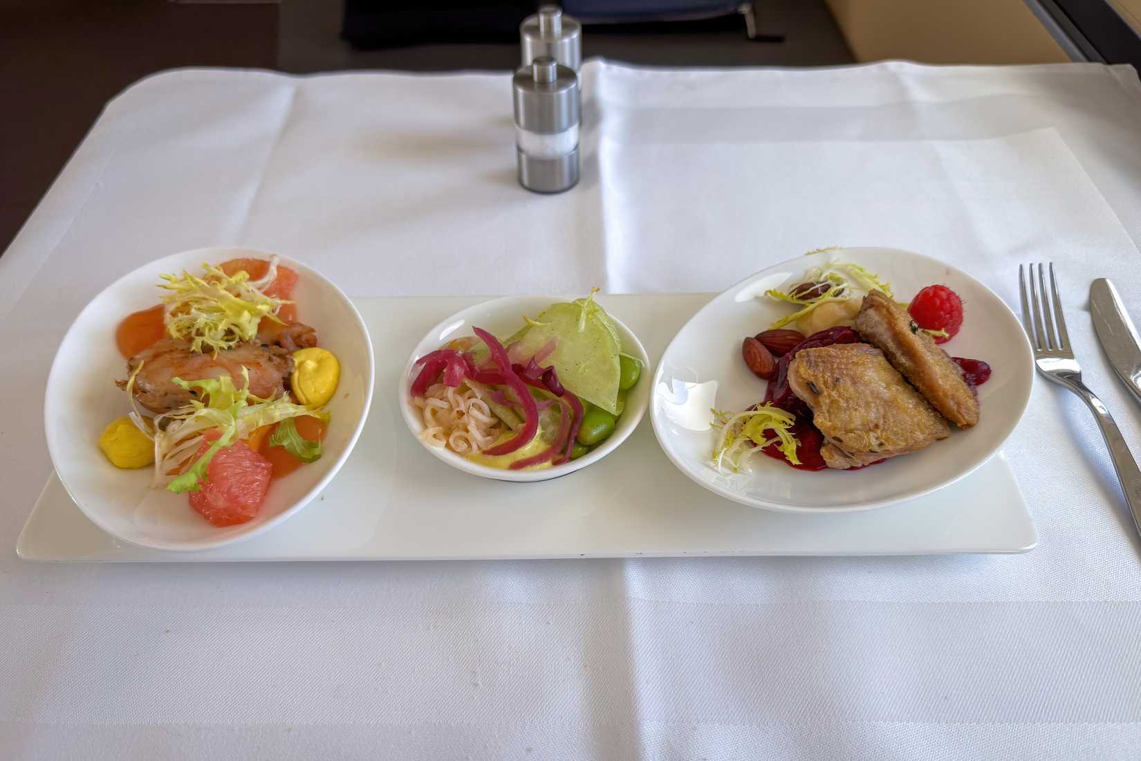 Munich, Germany - March 29, 2024:  Traveling Lufthansa First Class in an Airbus A380 - Starter service confitted shrimp (left), pickled kohlrabi (middle) and quail breast