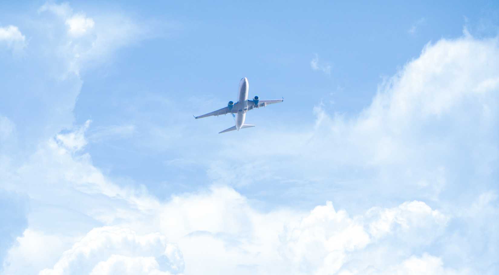 Front view of passenger airplane flying above fluffy white clouds in blue sky.