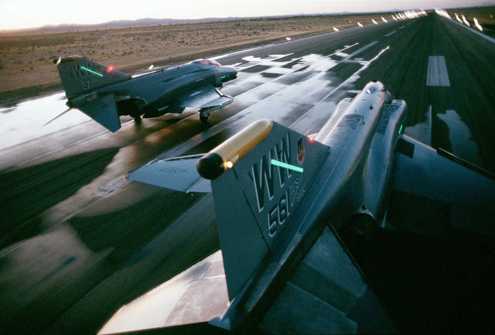 Two F-4G Wild Weasel Phantom II aircraft from the 37th Tactical Fighter Wing prepare for takeoff on the runway.