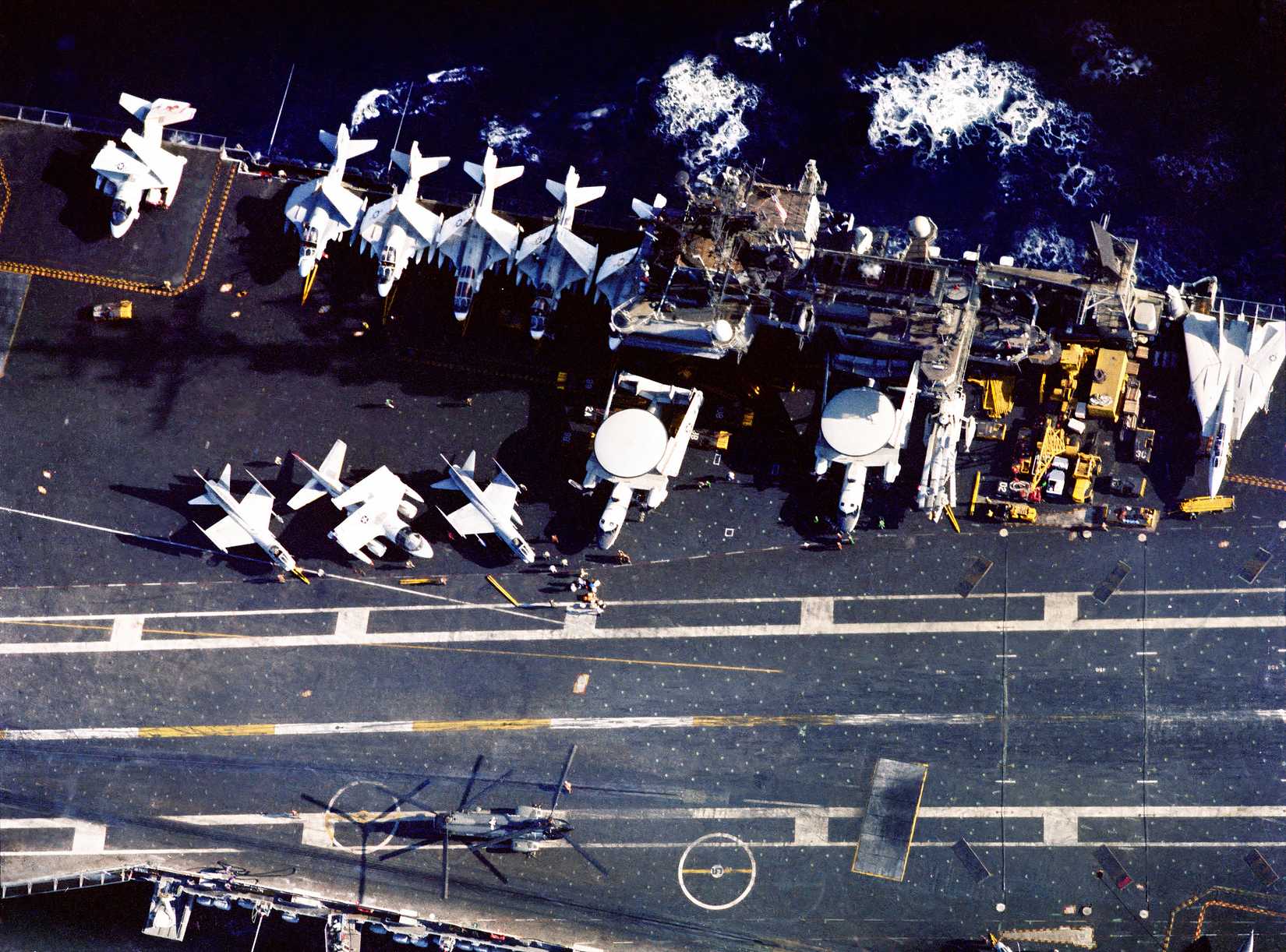 An overhead view of a deployed US aircraft carrier with aircraft on the deck. The aircraft include the S-3 Viking.