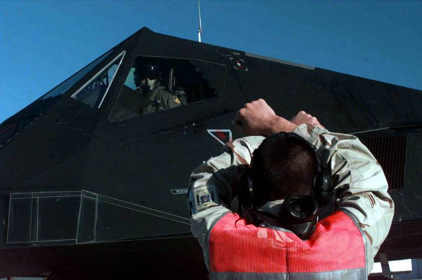 Airman 1st Class Emett Hamilton signals to Lt. Col. Doug Stewart in his F-117A Nighthawk as it parks on the ramp an operating base in Southwest Asia on Feb. 17, 1998. 