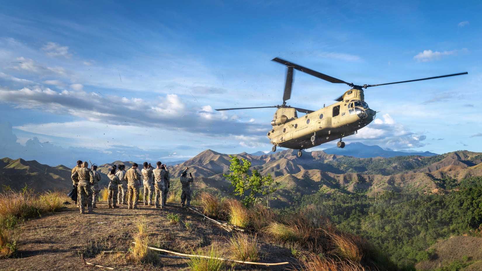 Army CH-47 Chinook helicopter assigned to Task Force Saber, 25th Combat Aviation Brigade, 25th Infantry Division, flies by U.S. Soldiers atop a mountain
