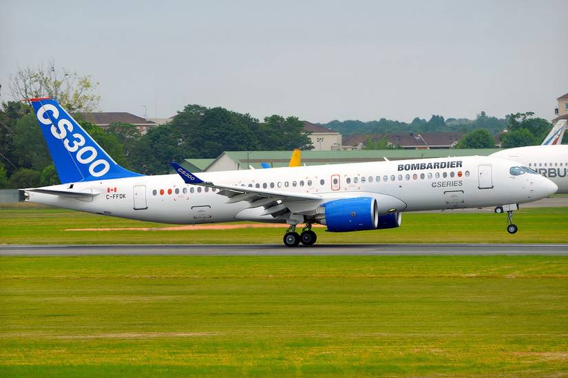 A Bombardier CSeries CS300 test aircraft on a runway, featuring a white fuselage with "BOMBARDIER CSERIES" branding, bright blue engine nacelles, and a vibrant blue tail fin with large white "CS300" text, set against a green airfield background.