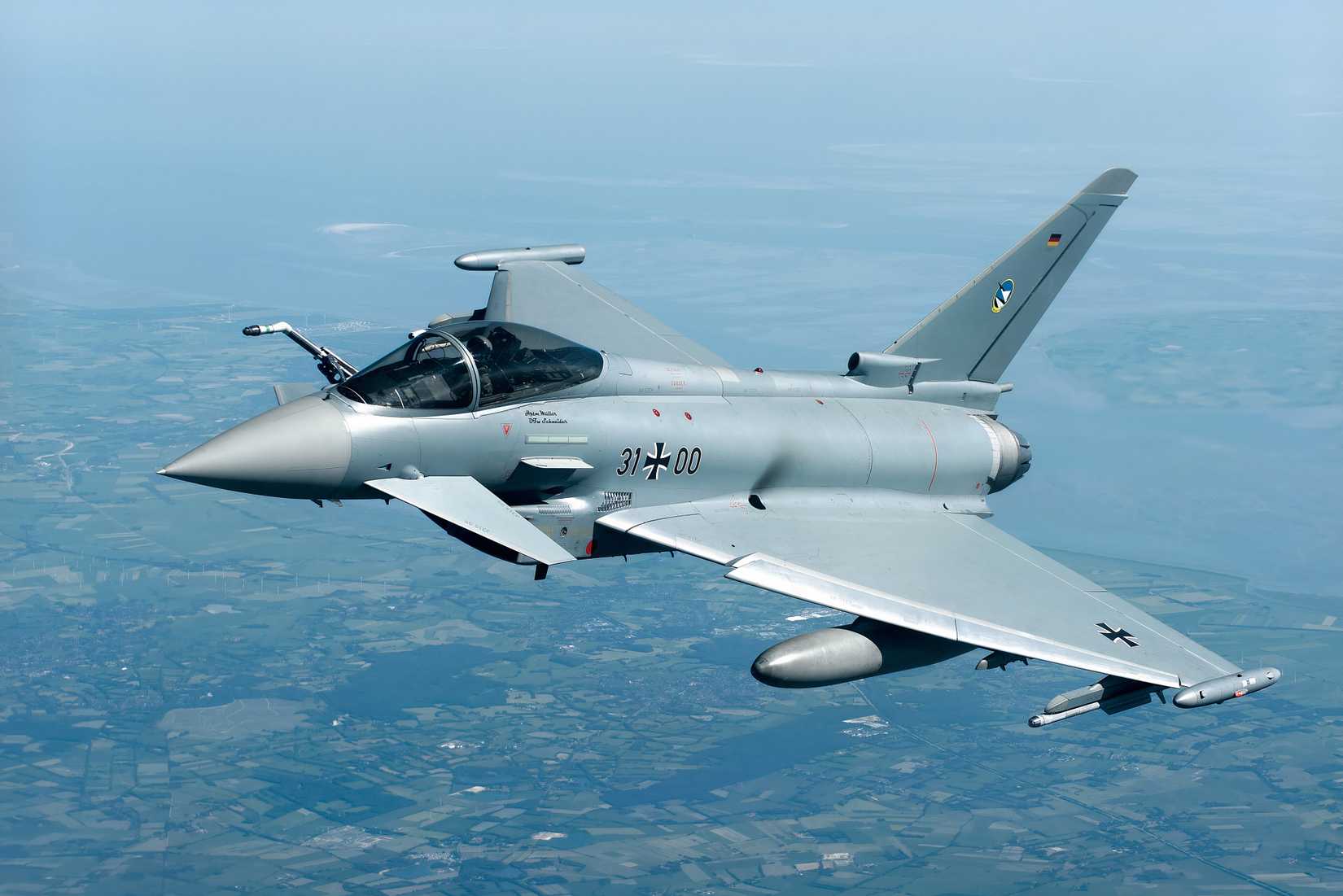 A photo of a Eurofighter flying over the countryside on a clear day.