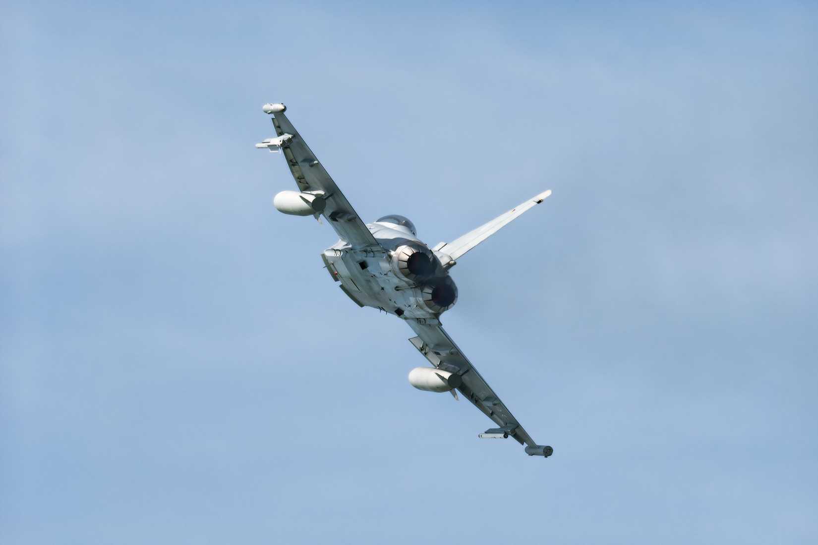 A photo of a Typhoon flying away from the viewer against a slightly overcast sky.