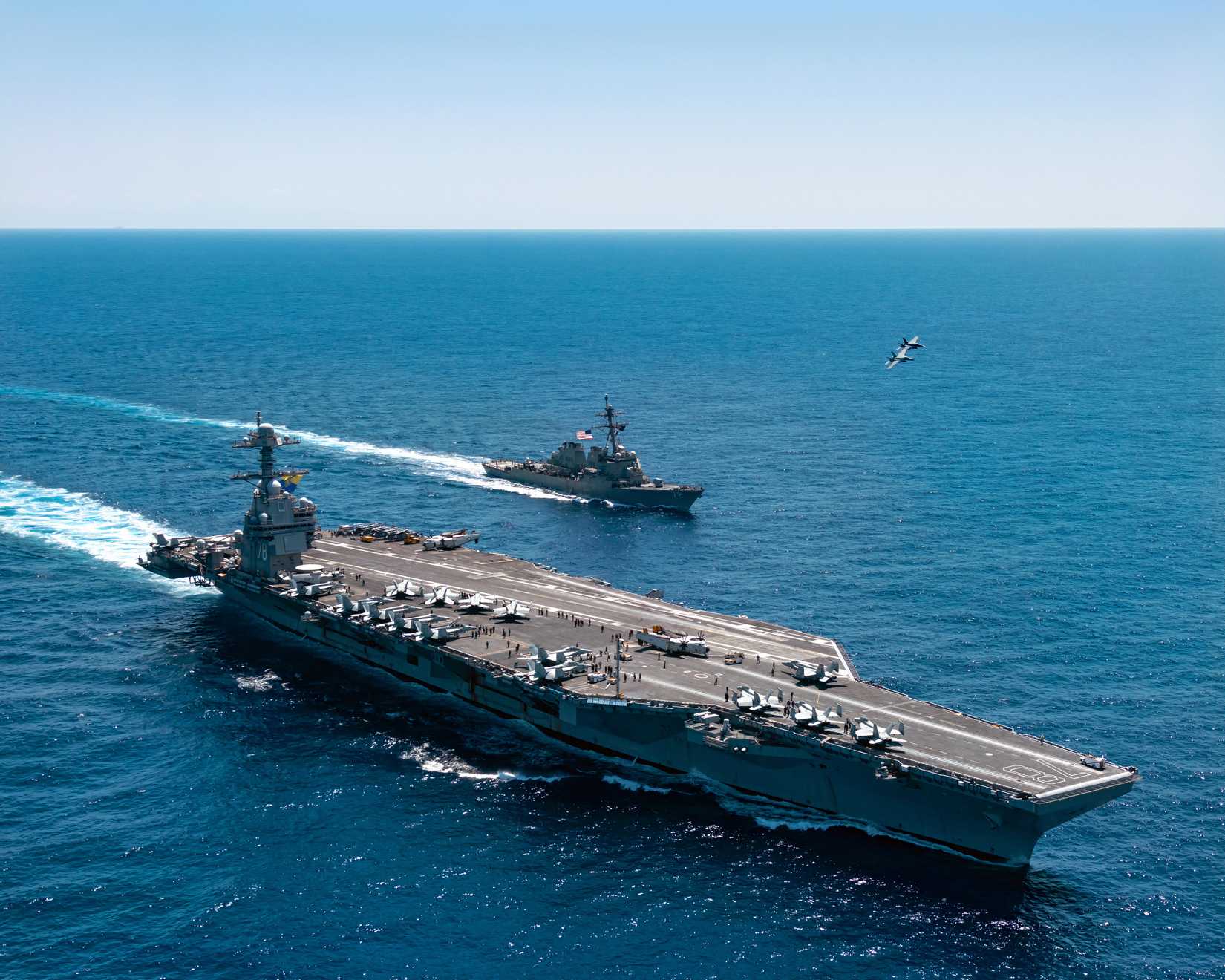 A photo of the USS Ford (CNV 78) operating at sea. On the deck of the carrier, carious aircraft and crew are visible.