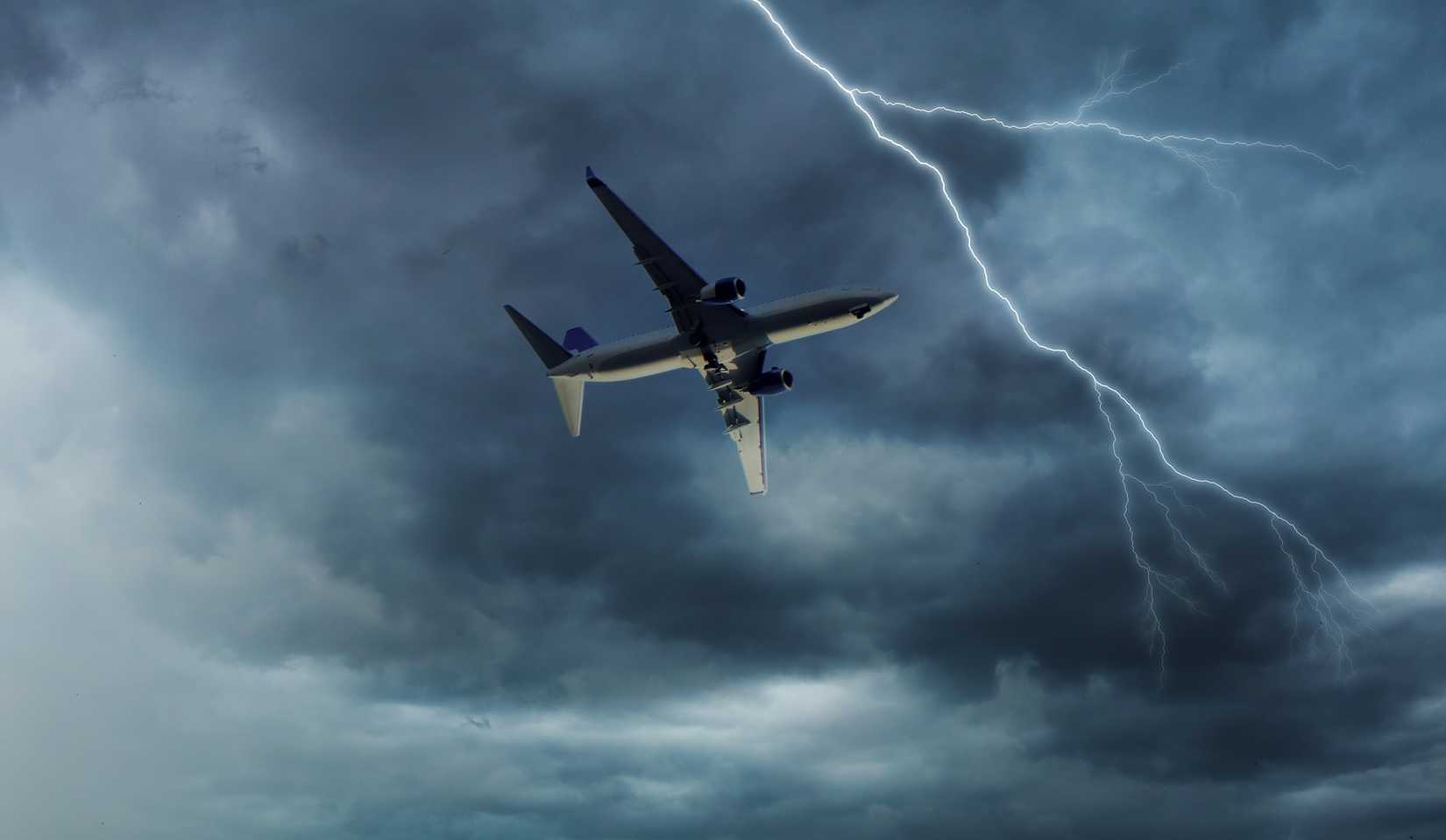 Airplane flying in stormy dark grey sky with thunder and lightning.
