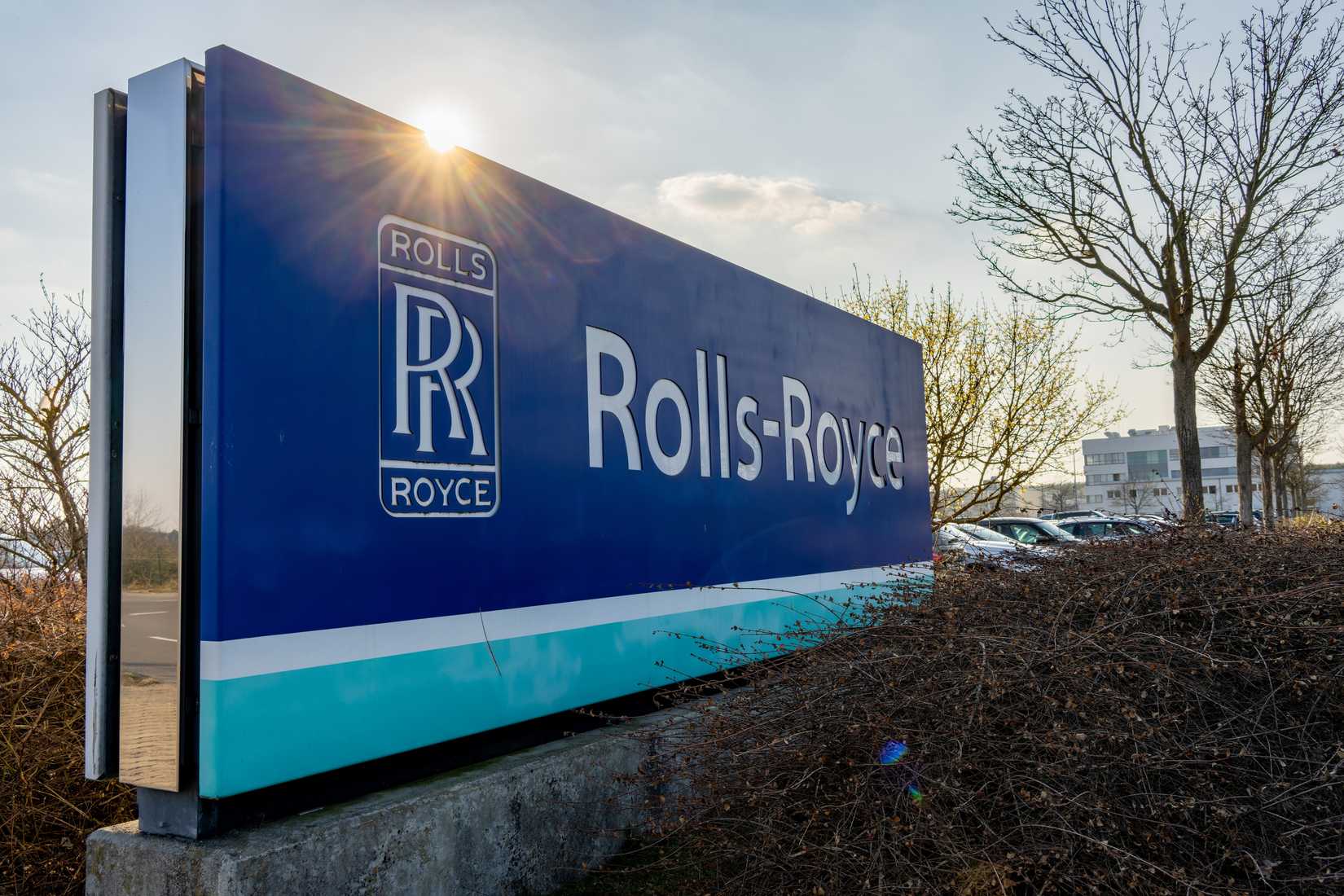 Sign with logo and company name of Rolls-Royce in front of the factory - sunbeams can be seen on top of the sign