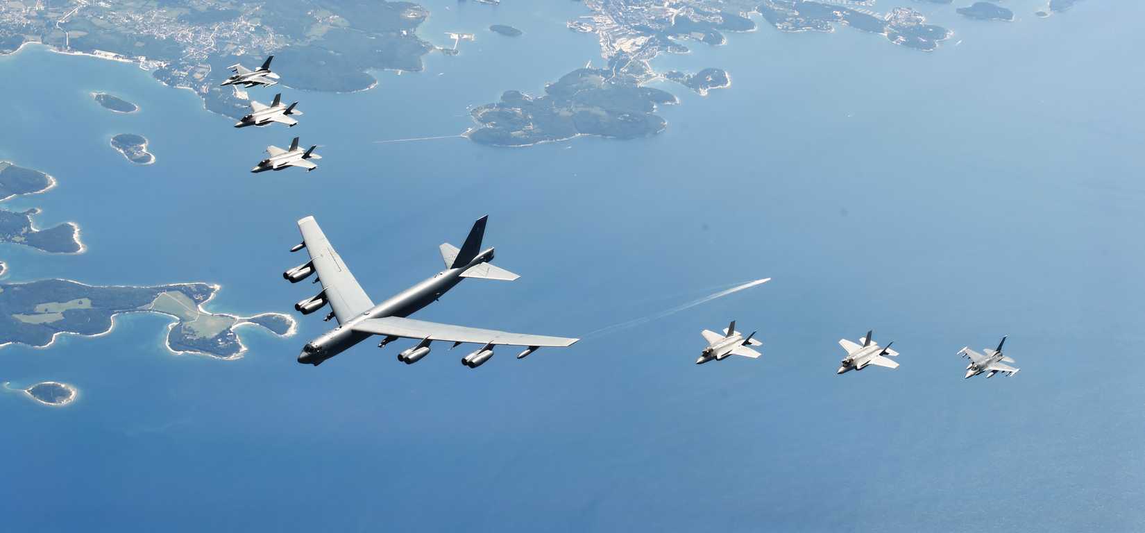 A photo of a B-52 flying with six flanking F-35s 