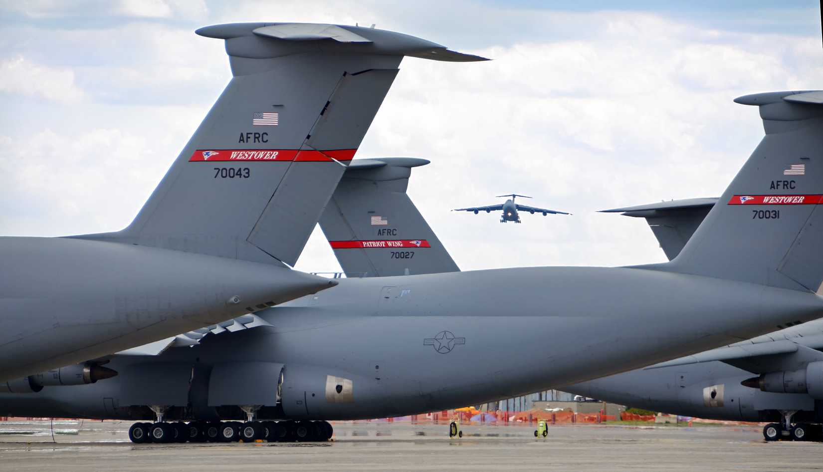 A photo showing a C-5 Galaxy making a landing in the background with several Galaxy tail-sections in the foreground.