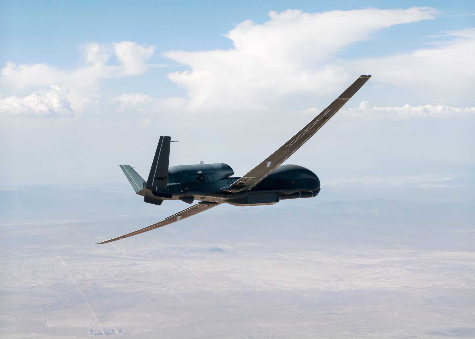 A photo of a Global Hawk drone flying over a desert. 