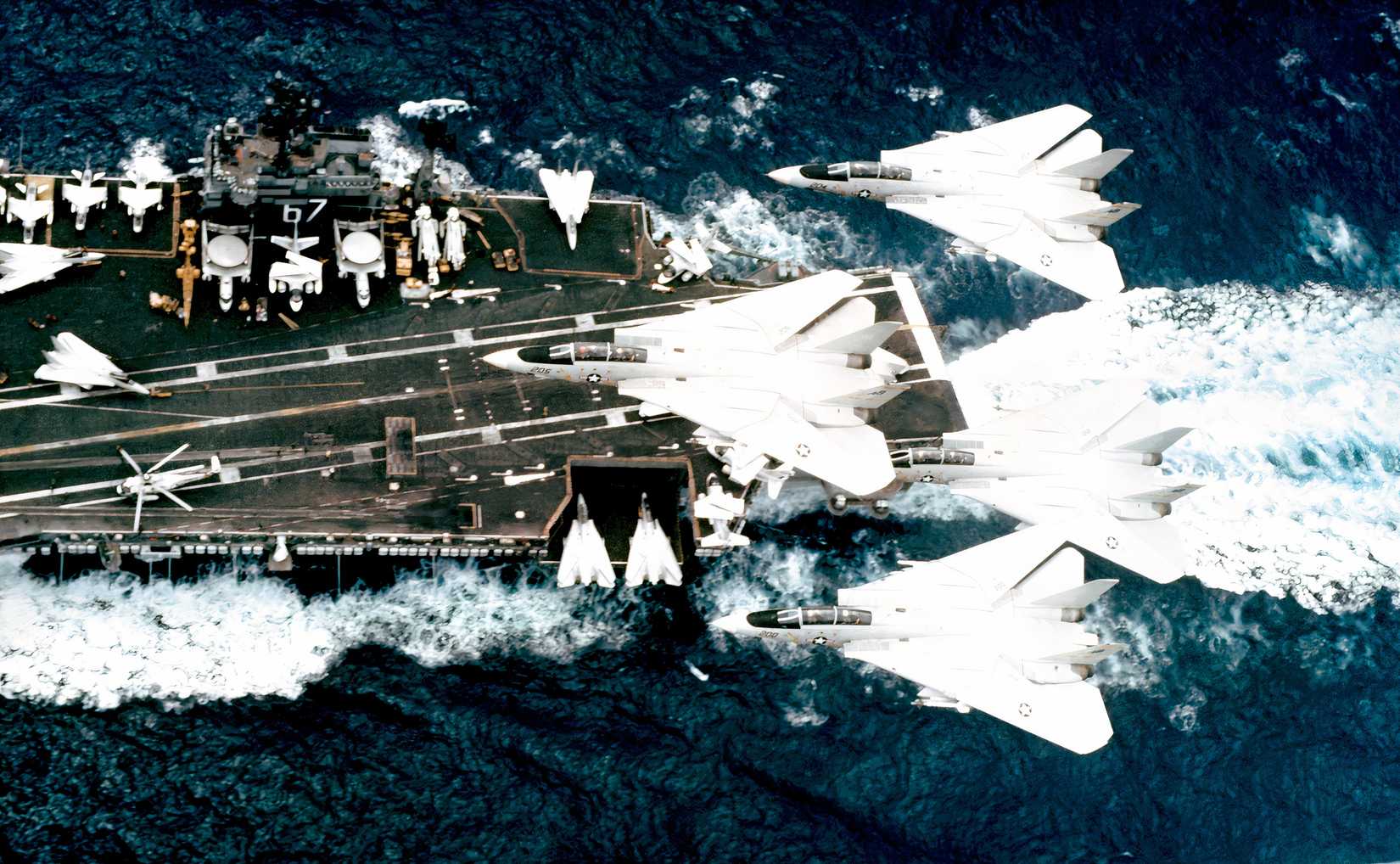 A photo of four F-14s flying over a carrier at sea.