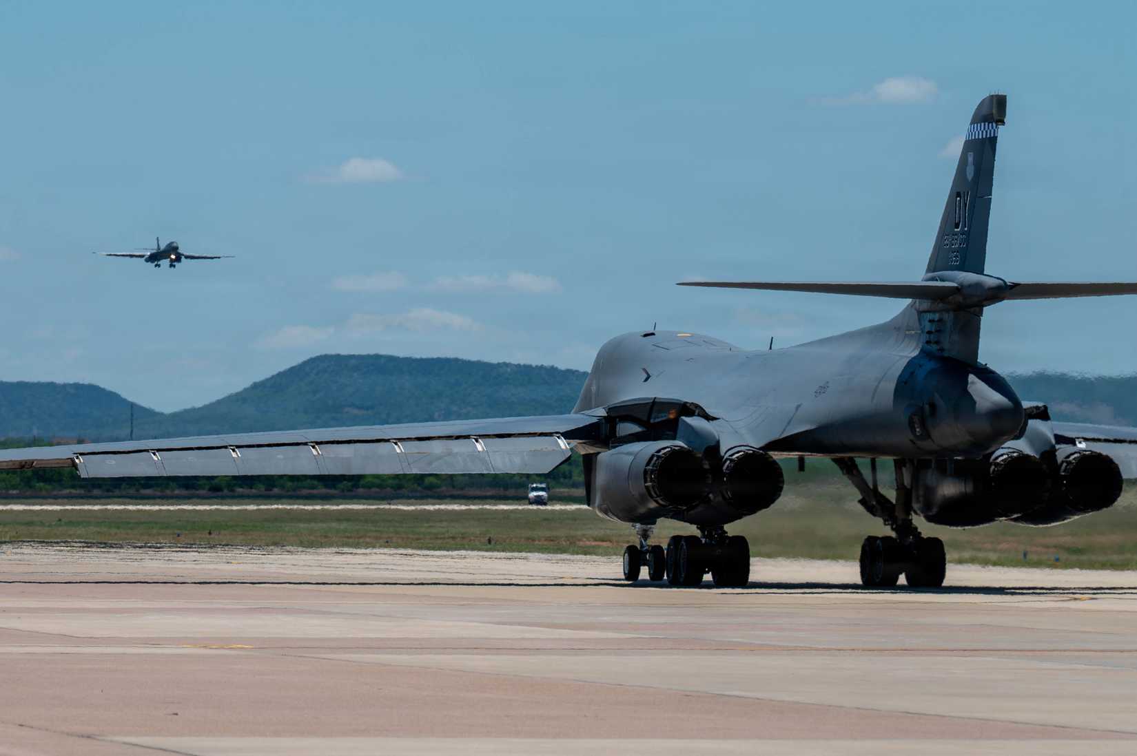 A B-1B Lancer assigned to the 7th Bomb Wing comes in for a landing as a 28th Bomb Squadron B-1B prepares for departure at Dyess Air Force Base, Texas
