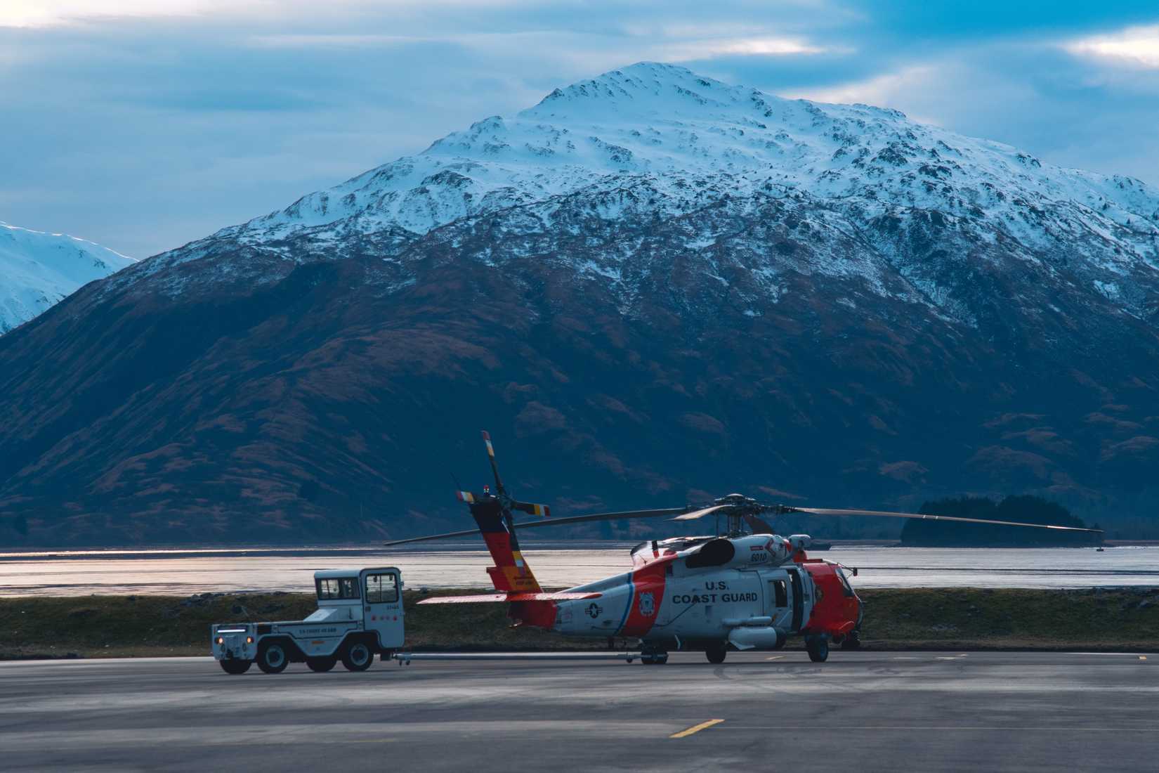 A Coast Guard aviator tows an Air Station Kodiak MH-60 Jayhawk helicopter on the air station's tarmac