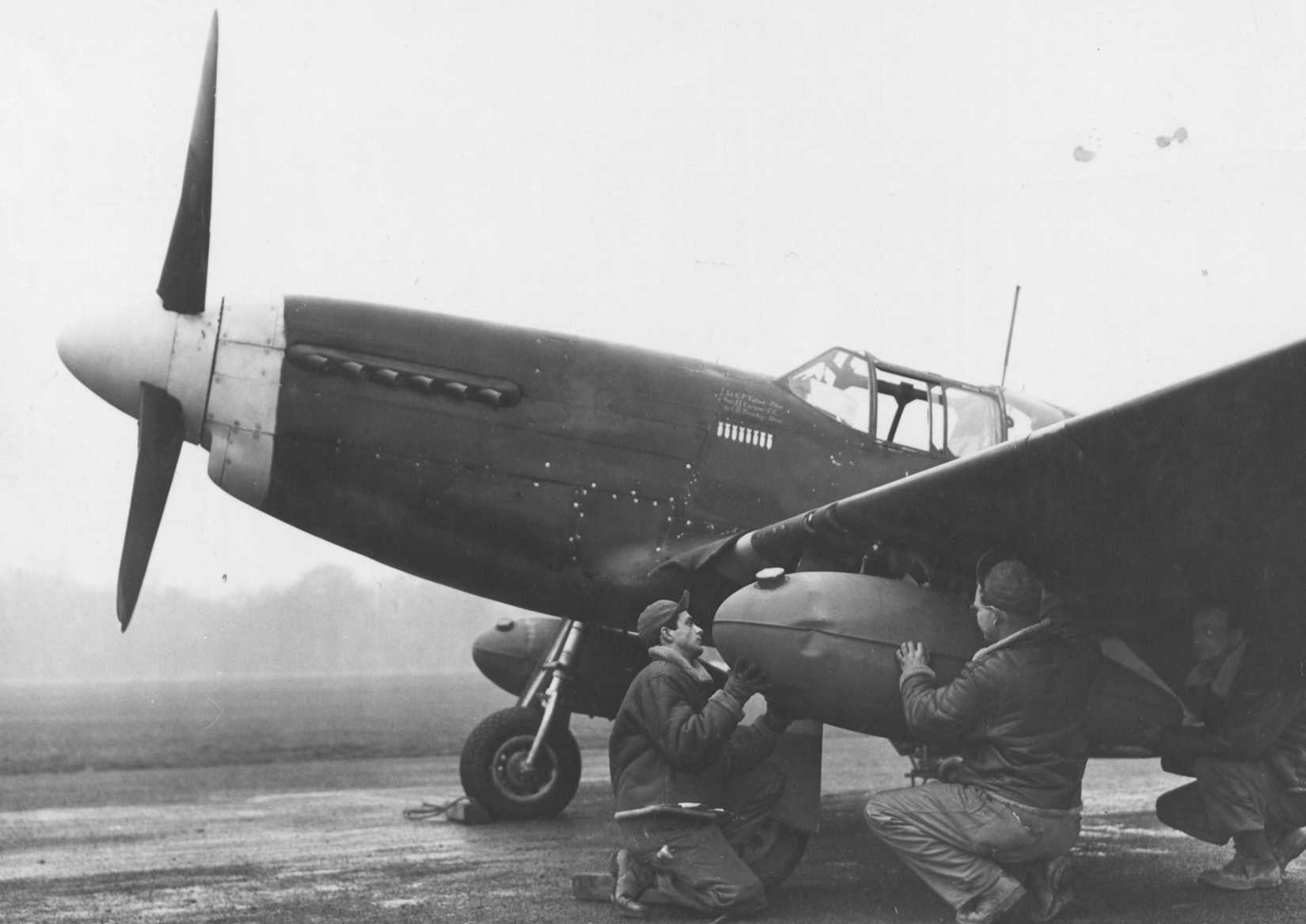 A ground crew fits an auxiliary gasoline tank to wing of a North American P-51 %22Mustang%22
