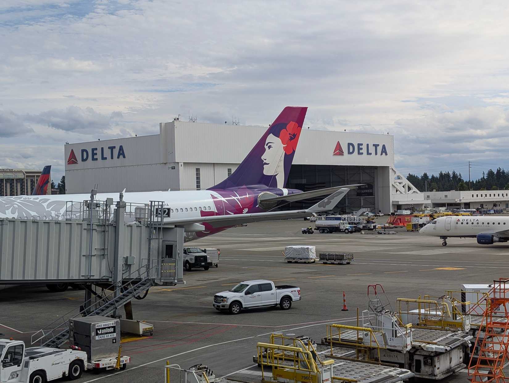 A Hawaiian Airlines aircraft parked in front of a Delta Air Lines hangar