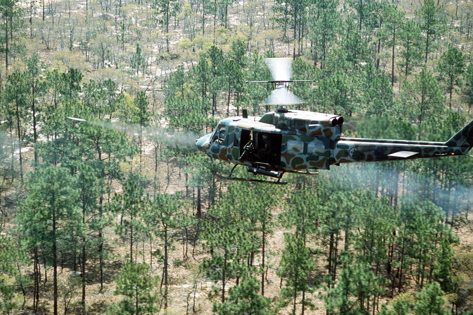 Air-to-Air left rear view of a UH-1N Iroquois helicopter with a camouflage paint scheme, as it performs low level rocket firing.