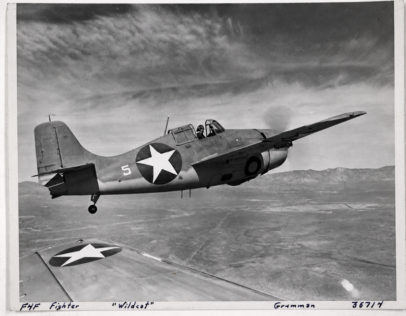 A photo of an F4F Wildcat flying with a partner aircraft over a desert. 