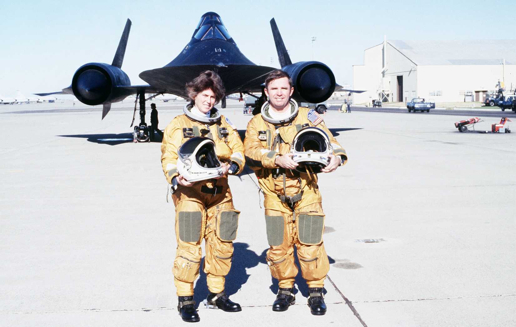 Representative Beverly B. Byron, Democrat-Maryland, poses with a pilot in front of an SR-71 aircraft after a demonstration flight. They are wearing flight suits designed especially for the SR-71