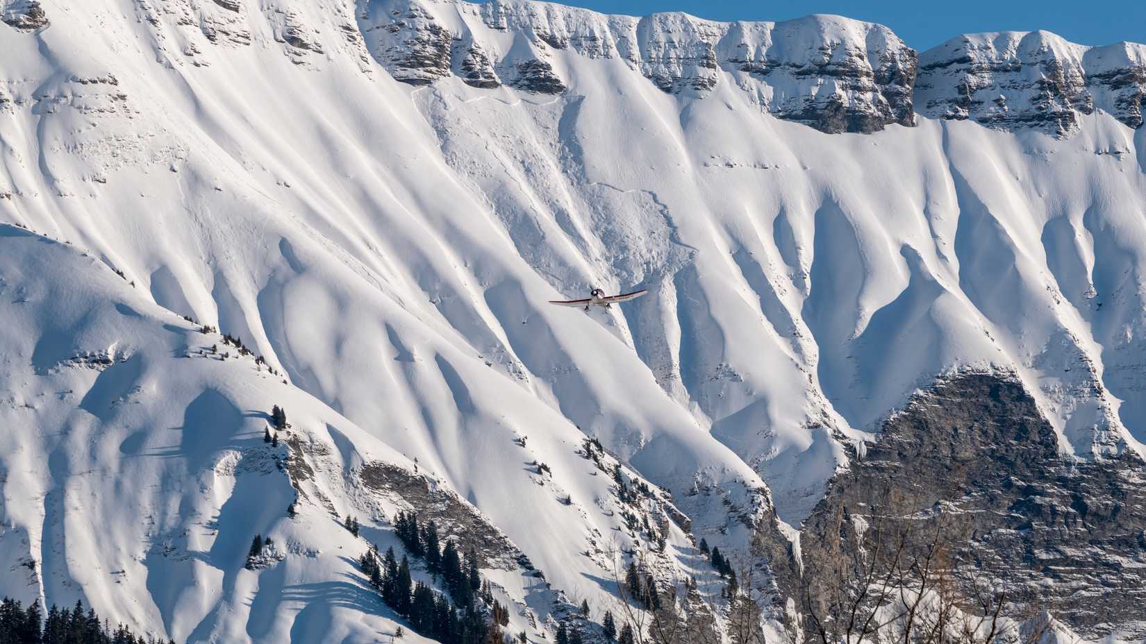  A small aircraft soars over snow-covered mountains, contrasting against the white snow.
