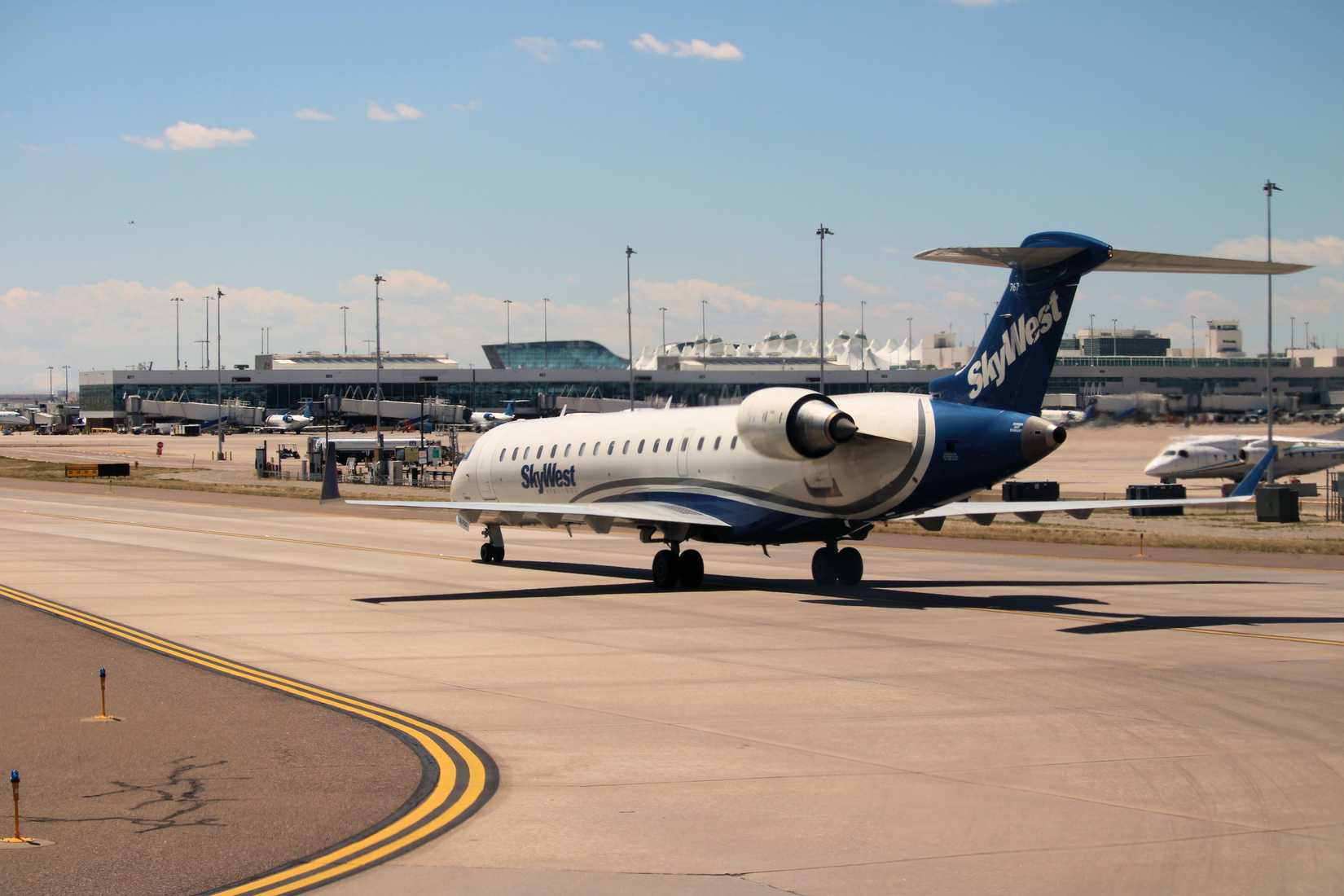 Skywest Airlines CRJ 700 aircraft taxiing to the gate with the main terminal and concourses beyond taken in the Denver, CO Intl Airport