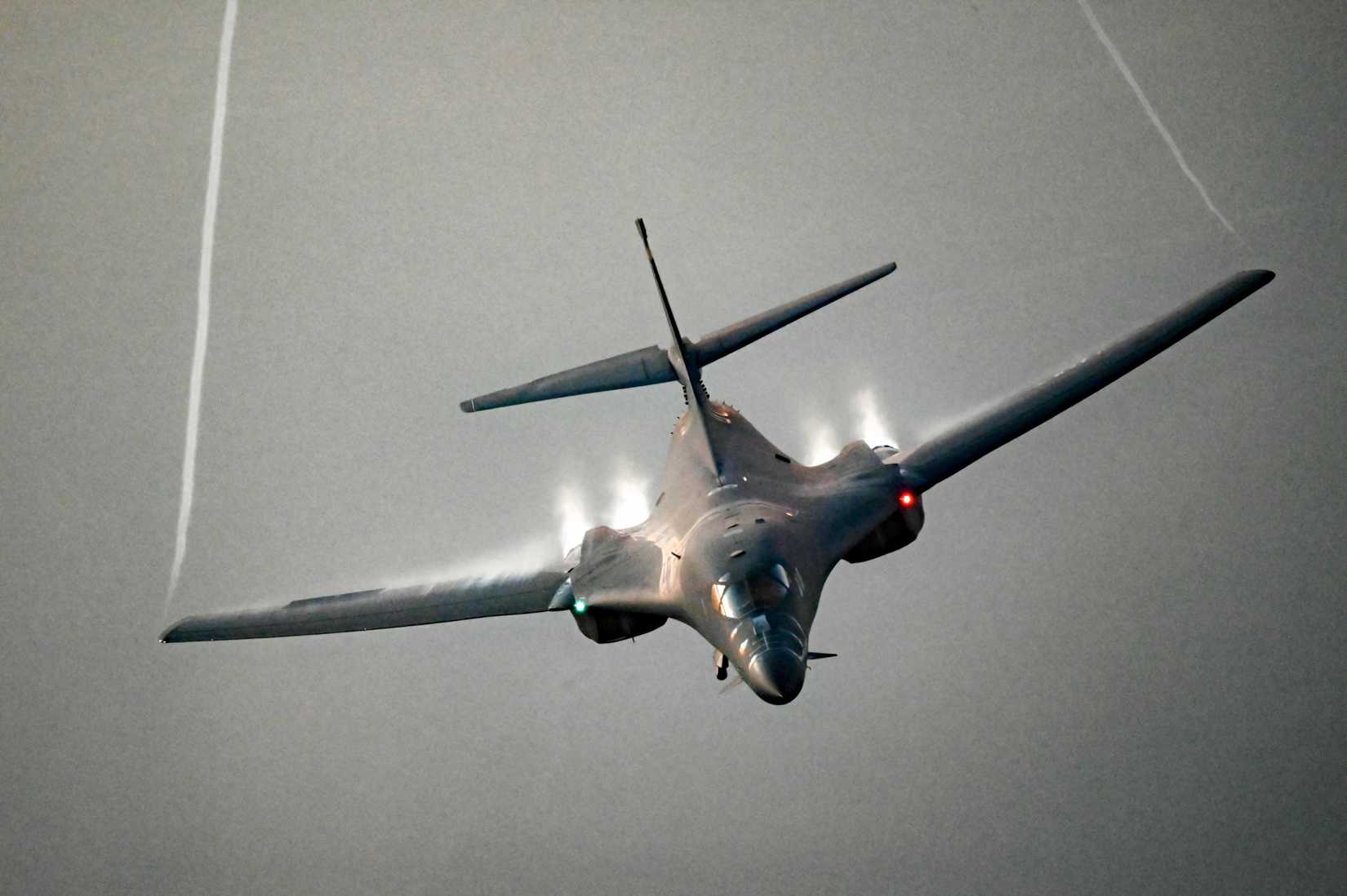 A photo of a B-1B flying toward the viewer against a grey background. 