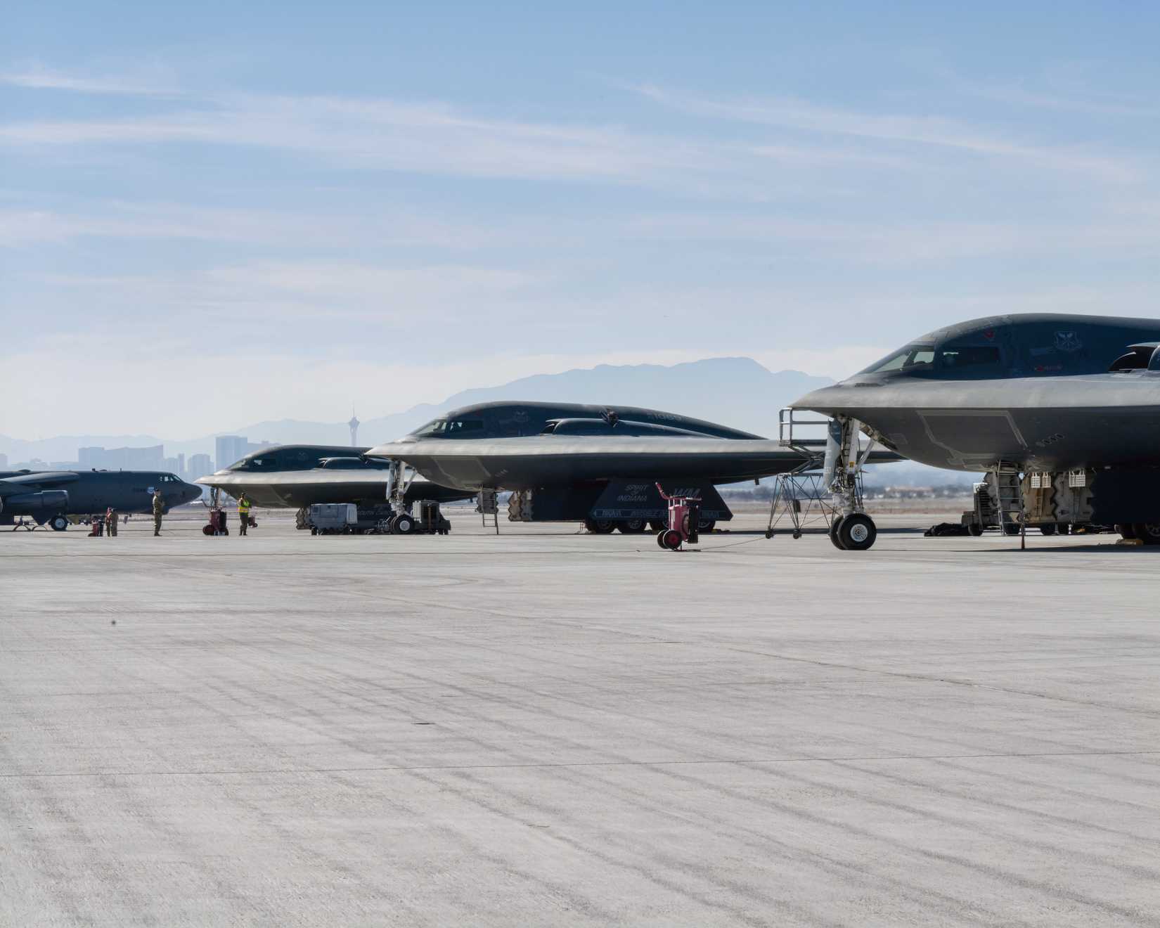 A photo of three B-2 bombers in the foreground with a B-52 in the background all parked on the tarmac at an airbase.
