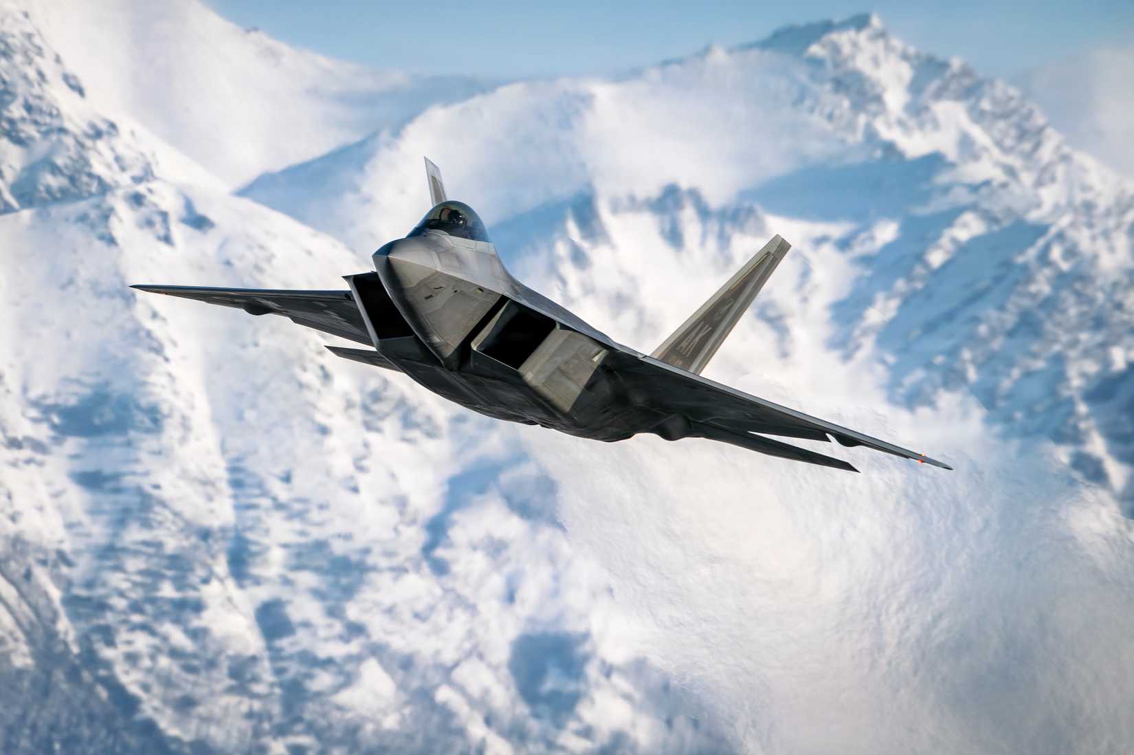 A photo of an F-22 flying forward towards the viewer with mountains in background.