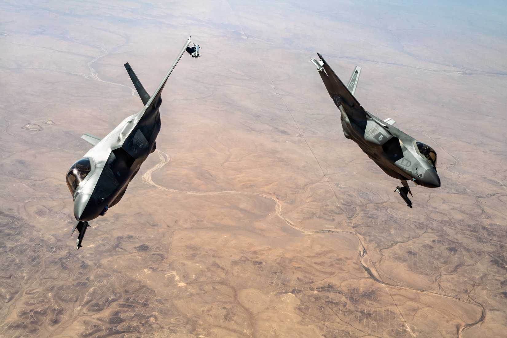 A pair of F-35s breaking away from each other while flying over a desert.