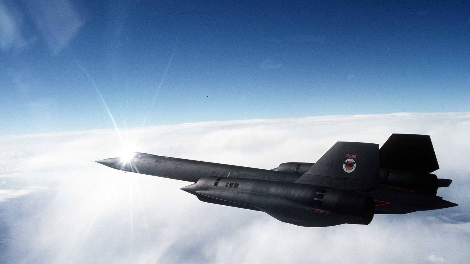 An air-to-air left side view of an SR-71 aircraft over cloud cover
