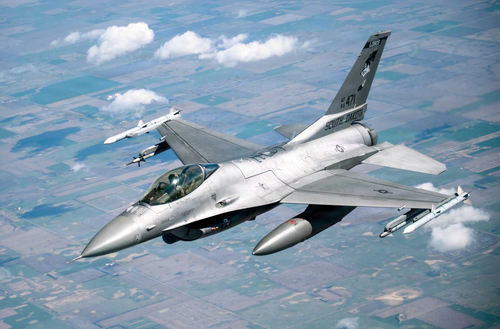 A clos-up photo of an F-16 flying ove a rural landscape.