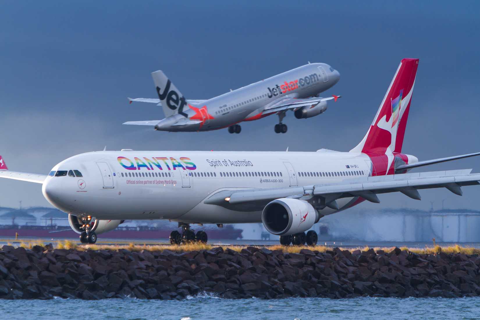 Sydney, New South Wales / Australia - April 28 2018: Qantas Airbus A330 airliner in Sydney Mardi Gras rainbow livery taxis on runway, with Jetstar A320 Airliner taking off in background.