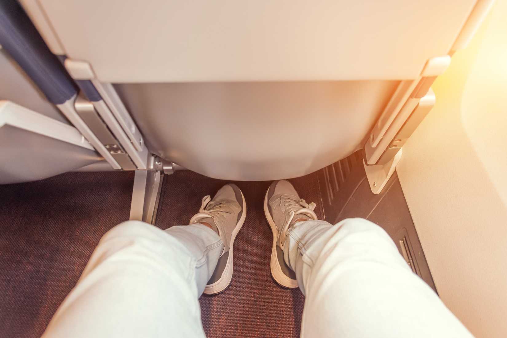 Enough legroom between the seats in the passenger plane, the view of the men's legs. Comfortable flight free space plus