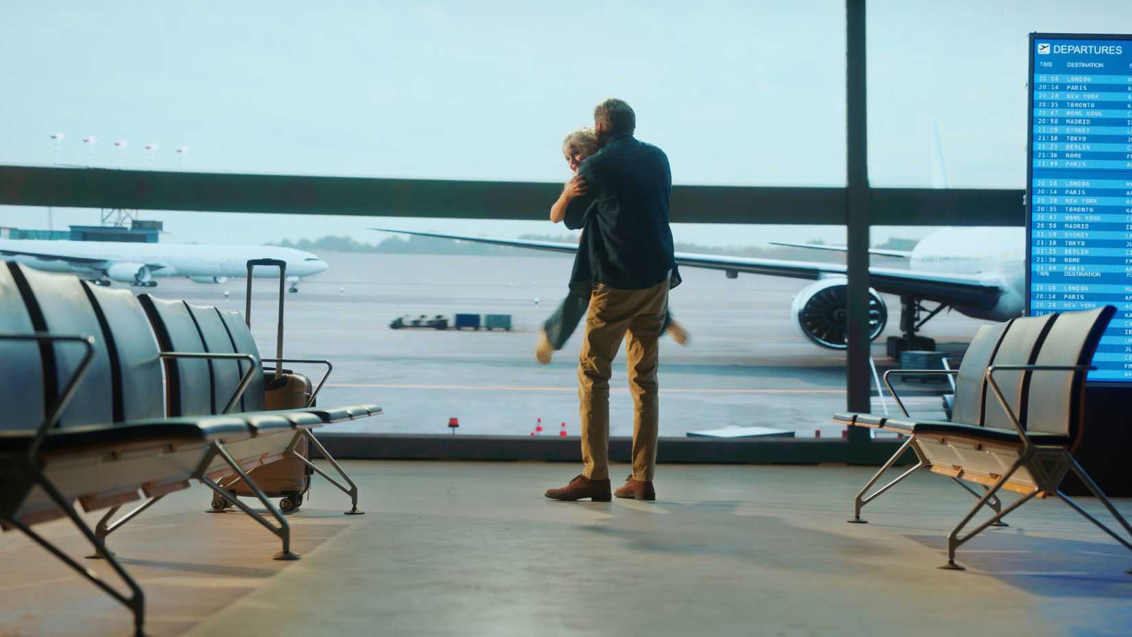 Father lifting and hugging daughter at airport lounge, near departure board, waiting for flight