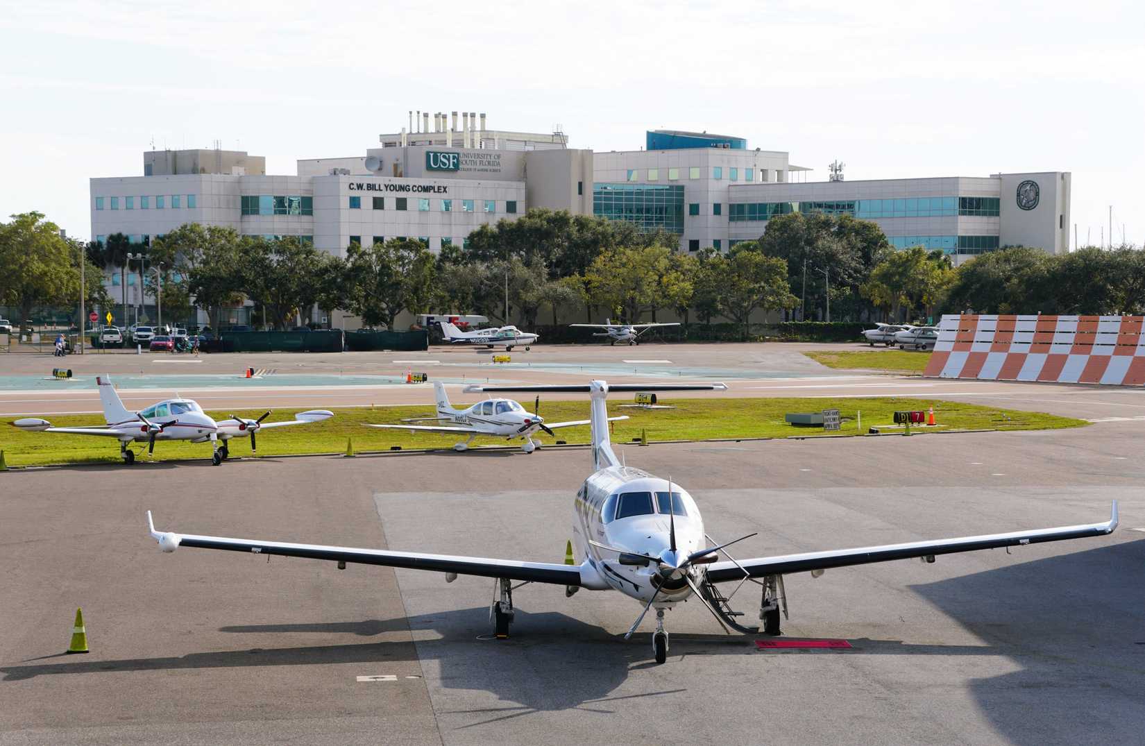 St Petersburg, Florida, U.S.A - Jan 2, 2026 - Several small private airplanes are parked on the tarmac at Albert Whitted Airport, with USF buildings in the background