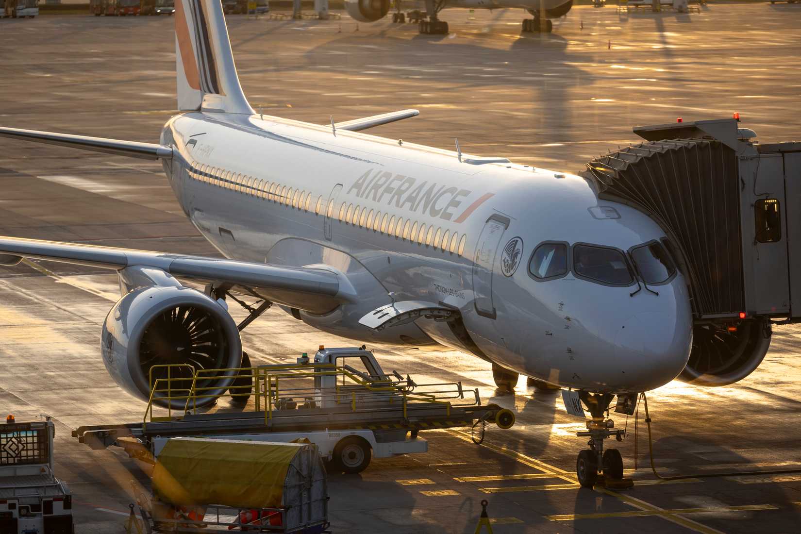 An Air France Airbus A220-300 docked at a jet bridge on the apron of Berlin Brandenburg Airport (BER) during sunset
