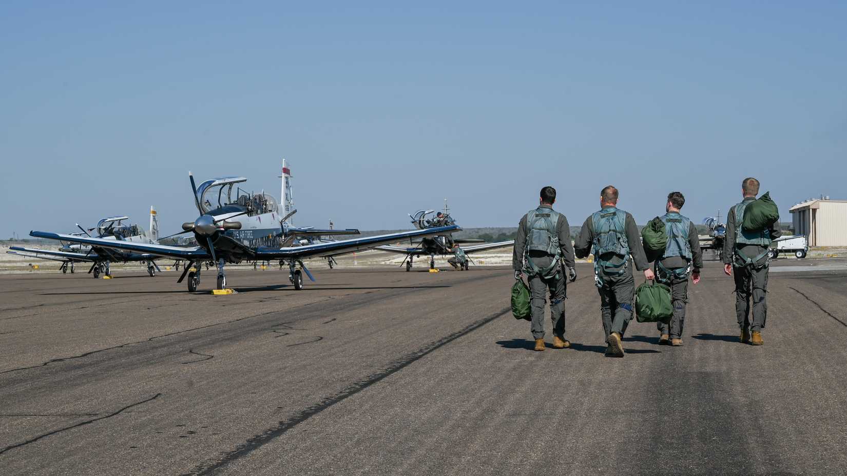 Student pilots and instructors walk along the flightline to their assigned planes during a training event at Del Rio International Airport