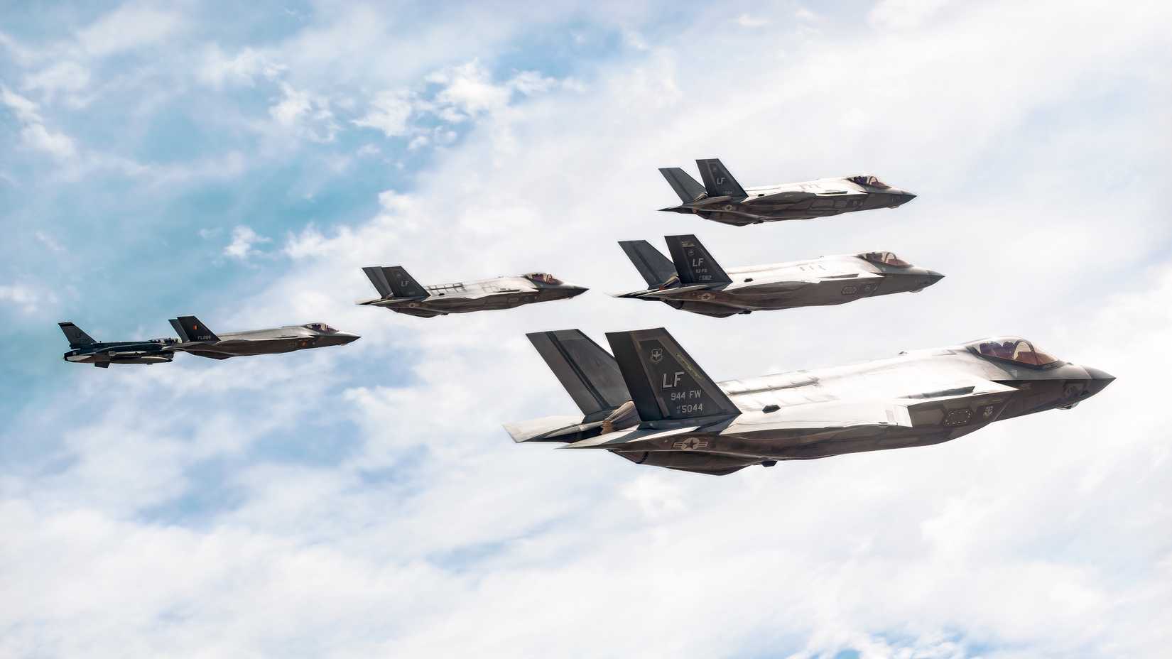 A group of six F-35s flying together against a background of clouds.