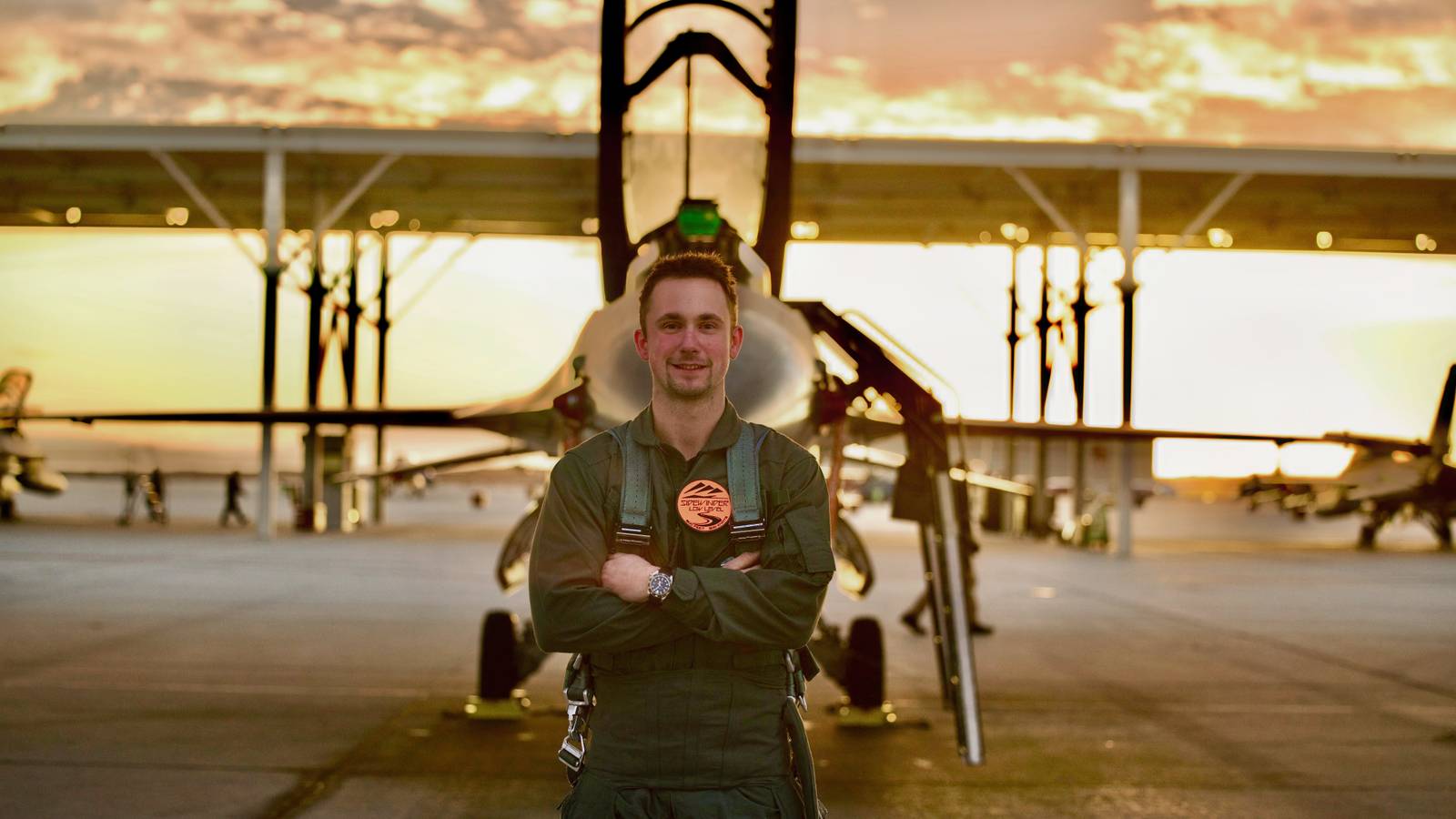 A photo of Louis Skupien standing in front of an F-16 with the sunset behind him.