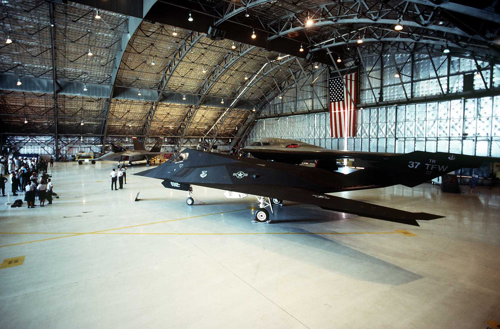 A 37th Tactical Fighter Wing F-117 aircraft stands in Hangar 3. The aircraft is part of a display which also includes the B-2 bomber F-22 fighter for Congressional viewing.