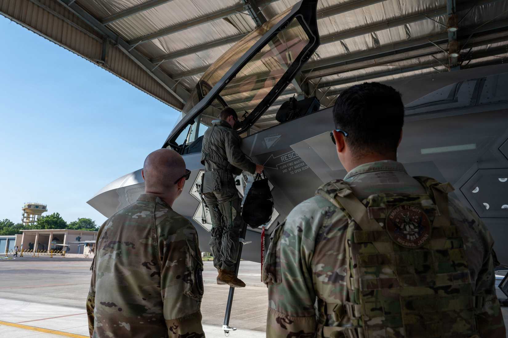 Air Force Airmen assigned to the 13th Aircraft Maintenance Unit and 35th Security Forces Squadron watch as an F-35A Lightning II pilot climbs into the aircraft