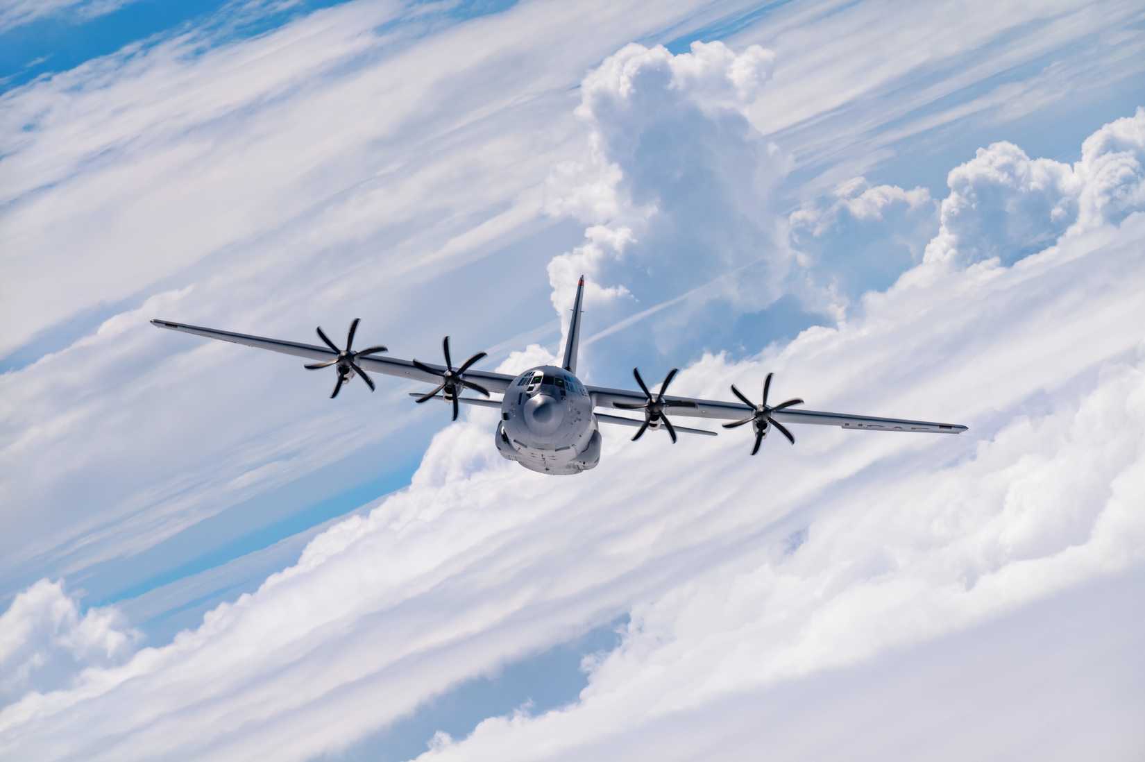 A photo of a C-130J flying with against a background of cloud formations.